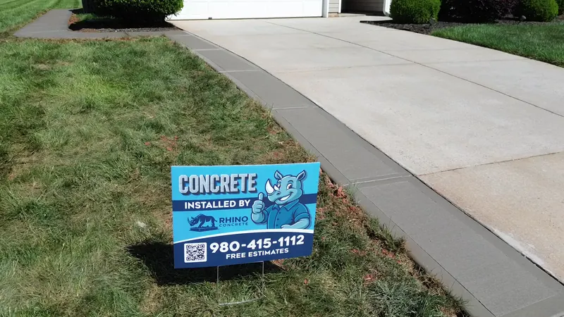 Finished concrete walkway along a driveway in Charlotte, with the Rhino yard sign